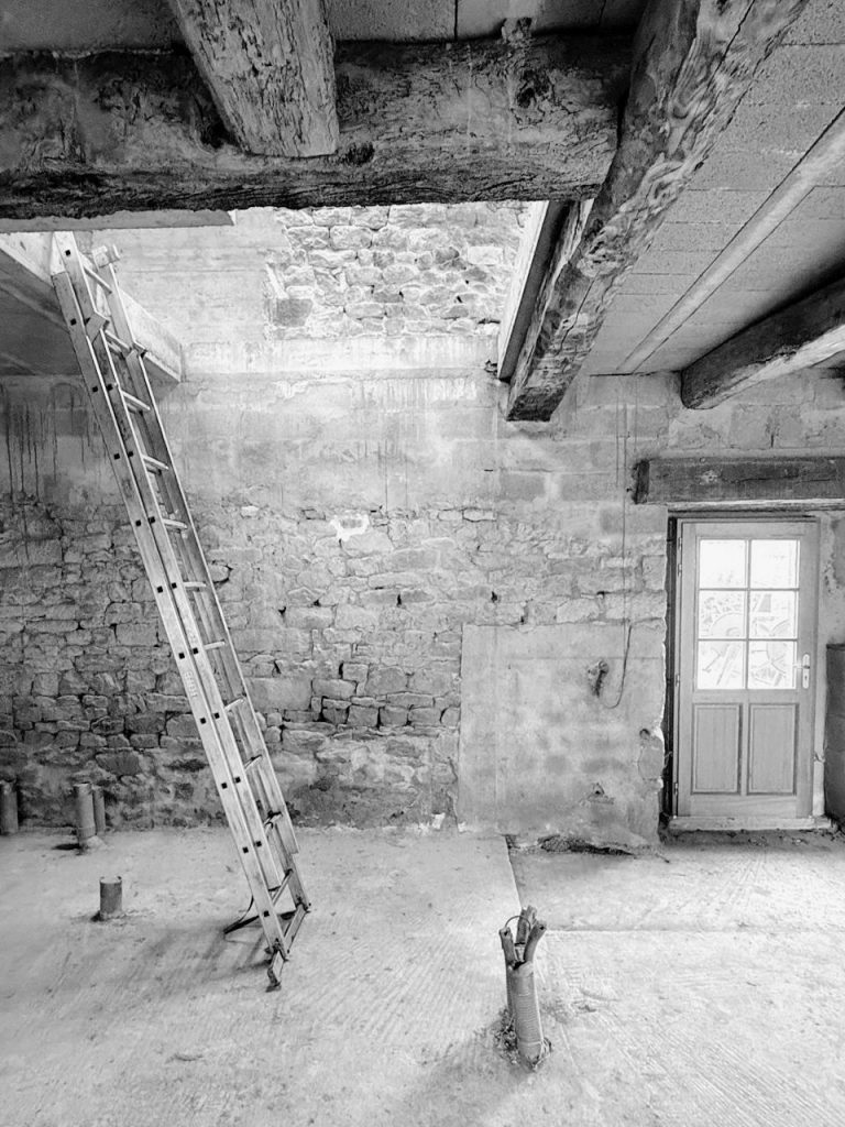 Intérieur brut d’une longère en pierre avec poutres anciennes et murs en pierre avant aménagement